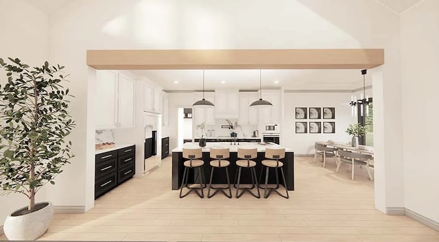 kitchen featuring stainless steel oven, a kitchen island with sink, decorative light fixtures, light hardwood / wood-style flooring, and white cabinetry