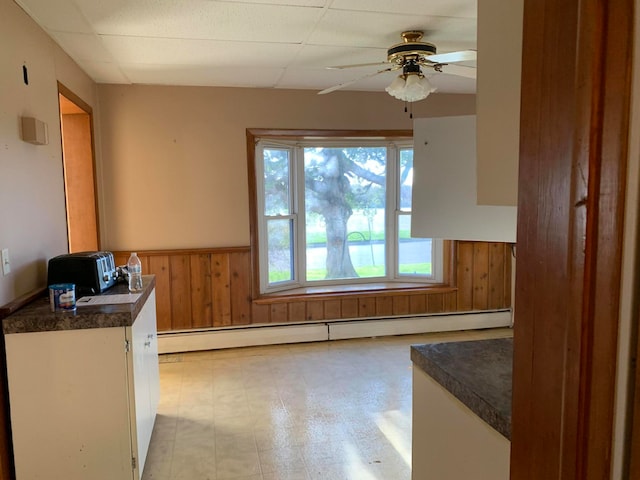 kitchen featuring a baseboard heating unit, a drop ceiling, ceiling fan, and wooden walls