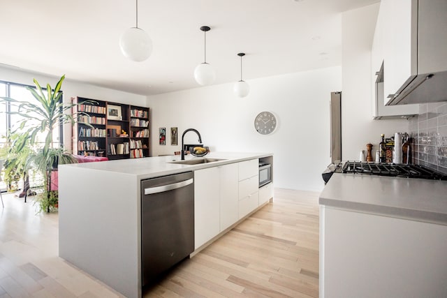 kitchen featuring sink, stainless steel appliances, an island with sink, decorative light fixtures, and white cabinets