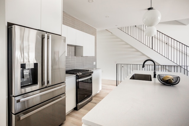 kitchen featuring stainless steel appliances, sink, pendant lighting, light hardwood / wood-style flooring, and white cabinetry