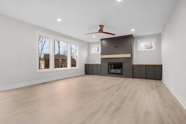 unfurnished living room featuring a large fireplace, ceiling fan, light hardwood / wood-style floors, and a healthy amount of sunlight