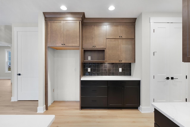 kitchen featuring light hardwood / wood-style floors, backsplash, light stone counters, and dark brown cabinetry