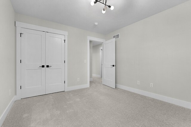 unfurnished bedroom with a closet, light carpet, and an inviting chandelier