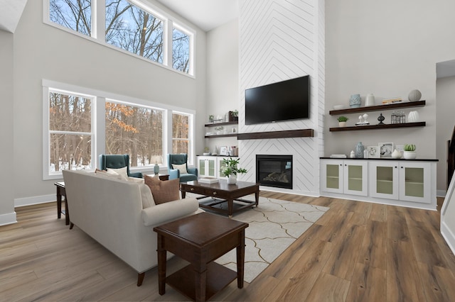 living room featuring a fireplace, a towering ceiling, baseboards, and wood finished floors