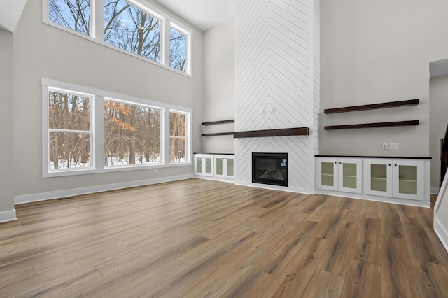 unfurnished living room featuring a fireplace, wood finished floors, a towering ceiling, and baseboards