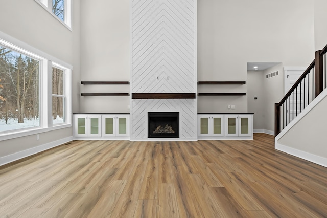 unfurnished living room featuring stairs, light wood-type flooring, a high ceiling, and a fireplace