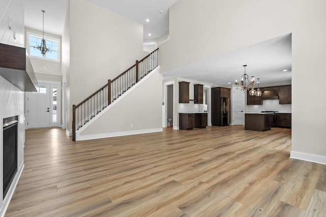 unfurnished living room with baseboards, a towering ceiling, stairway, light wood-type flooring, and a notable chandelier