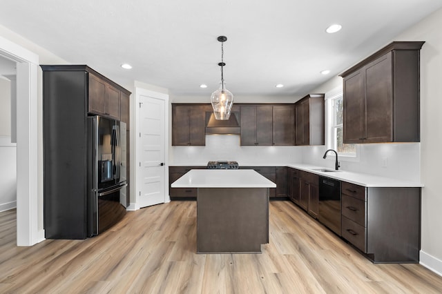 kitchen featuring a center island, light countertops, black appliances, pendant lighting, and a sink