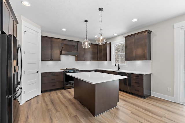 kitchen featuring a center island, custom exhaust hood, stainless steel appliances, light countertops, and hanging light fixtures