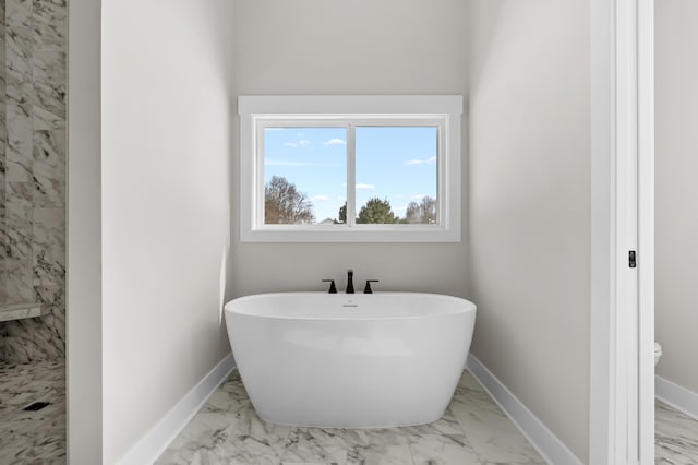 bathroom featuring marble finish floor, baseboards, and a soaking tub