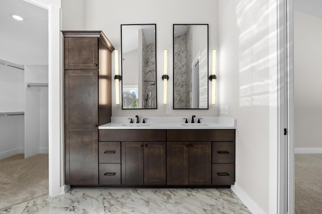 full bathroom with a spacious closet, double vanity, a sink, and baseboards