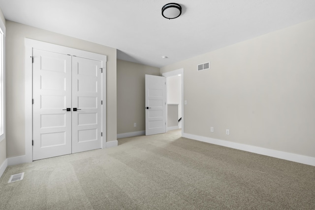 unfurnished bedroom featuring baseboards, visible vents, a closet, and light colored carpet