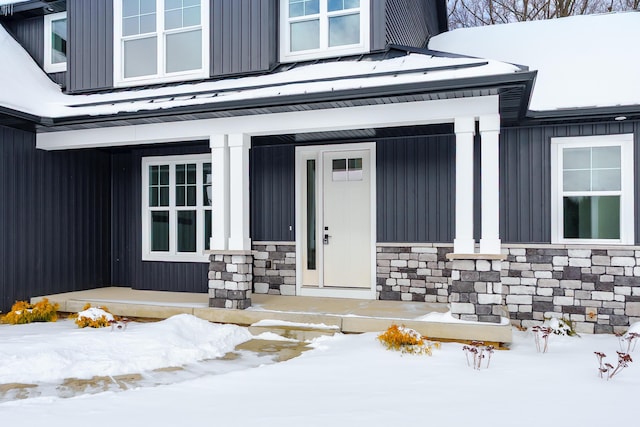 snow covered property entrance featuring board and batten siding and stone siding