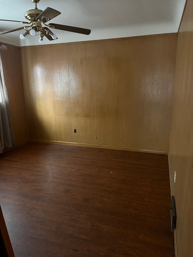 empty room with dark hardwood / wood-style floors, ceiling fan, and wood walls