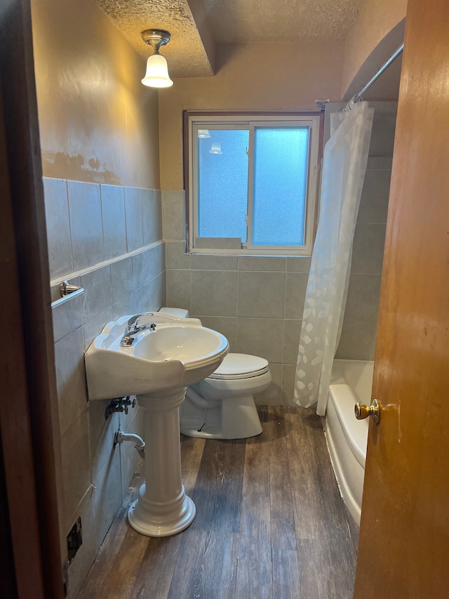 bathroom featuring shower / bath combo, a textured ceiling, tile walls, hardwood / wood-style floors, and toilet