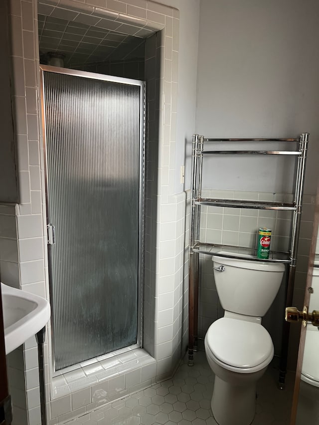 bathroom featuring tile patterned flooring, a shower with door, tile walls, and toilet