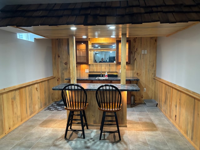 bar featuring sink, light tile patterned floors, and wood walls