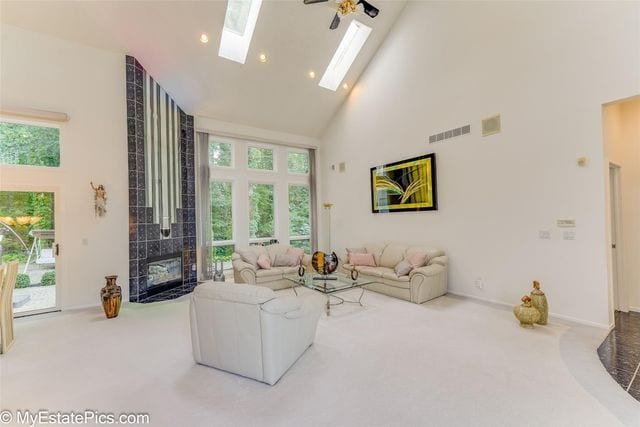 living room featuring carpet floors, a skylight, high vaulted ceiling, and ceiling fan