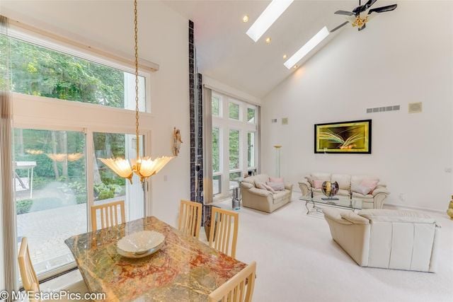 dining area with ceiling fan, carpet floors, high vaulted ceiling, and a skylight