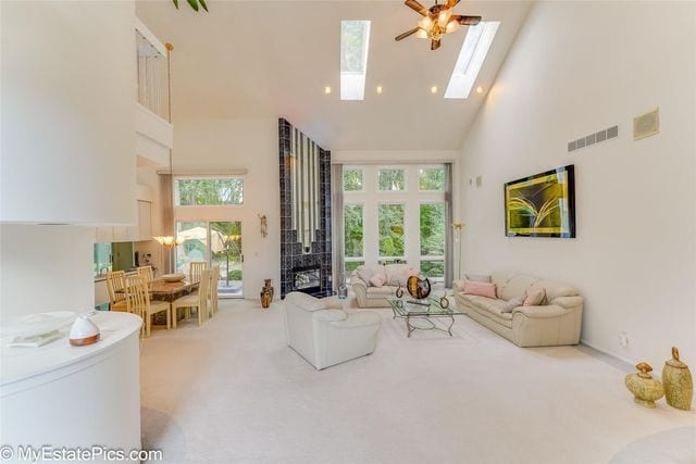 living room featuring a wealth of natural light, ceiling fan, light colored carpet, and high vaulted ceiling