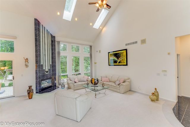 carpeted living room with ceiling fan, a tile fireplace, high vaulted ceiling, and a skylight