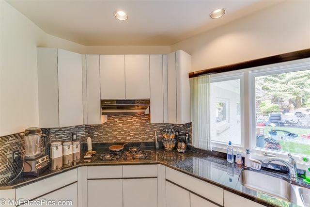 kitchen with decorative backsplash, white cabinetry, dark stone countertops, and sink