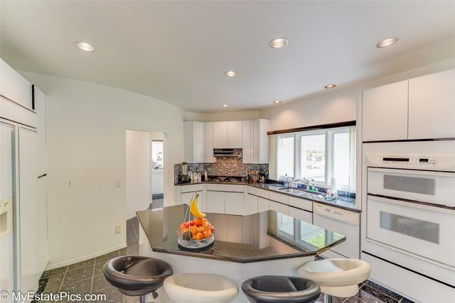 kitchen with a breakfast bar, white appliances, backsplash, white cabinets, and sink