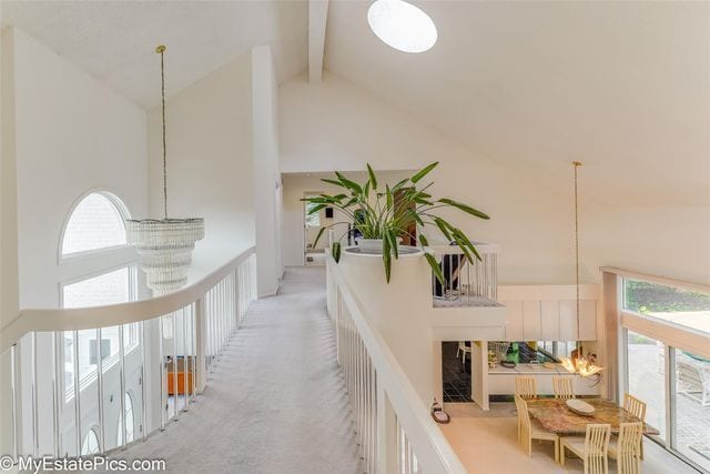 hall featuring beamed ceiling, a wealth of natural light, light carpet, and high vaulted ceiling