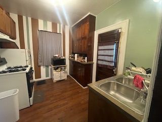 kitchen with white gas stove, dark wood-type flooring, and sink