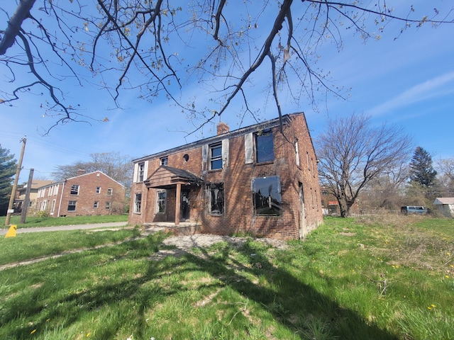 view of front of house featuring brick siding, a chimney, and a front yard