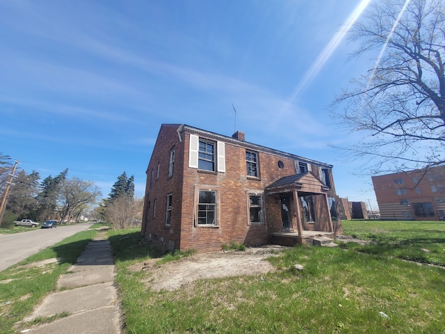 rear view of property featuring brick siding, a yard, and a chimney