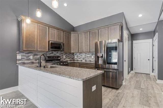 kitchen featuring kitchen peninsula, appliances with stainless steel finishes, light stone counters, light hardwood / wood-style floors, and lofted ceiling