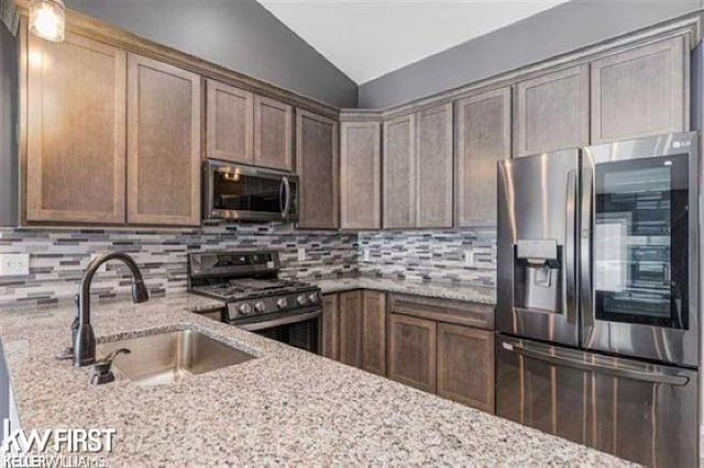 kitchen with light stone countertops, appliances with stainless steel finishes, tasteful backsplash, sink, and lofted ceiling