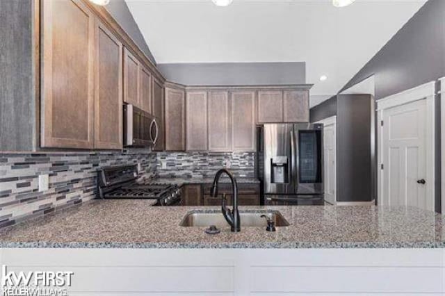 kitchen featuring sink, vaulted ceiling, light stone countertops, tasteful backsplash, and stainless steel appliances