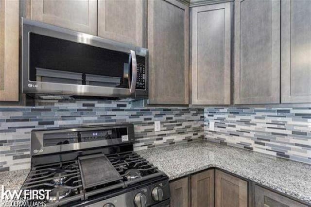 kitchen with black gas range oven, backsplash, and light stone counters