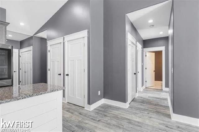 interior space featuring lofted ceiling, light hardwood / wood-style floors, white cabinetry, and dark stone counters