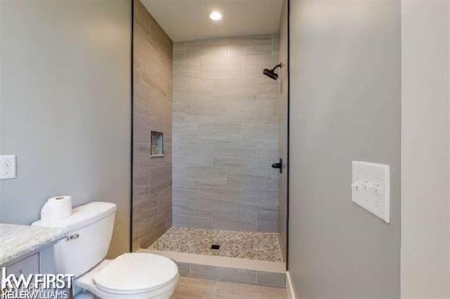 bathroom featuring tile patterned flooring, vanity, toilet, and tiled shower