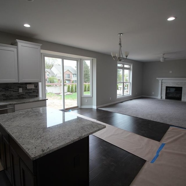 kitchen with pendant lighting, white cabinets, light stone counters, tasteful backsplash, and dark hardwood / wood-style flooring