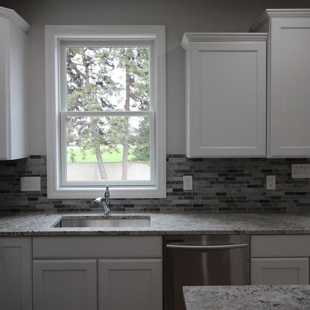 kitchen featuring white cabinets, light stone counters, stainless steel dishwasher, and sink