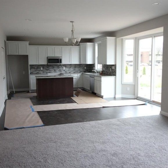 kitchen featuring appliances with stainless steel finishes, tasteful backsplash, a notable chandelier, white cabinets, and hanging light fixtures