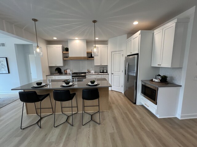 kitchen with an island with sink, white cabinets, hanging light fixtures, and appliances with stainless steel finishes