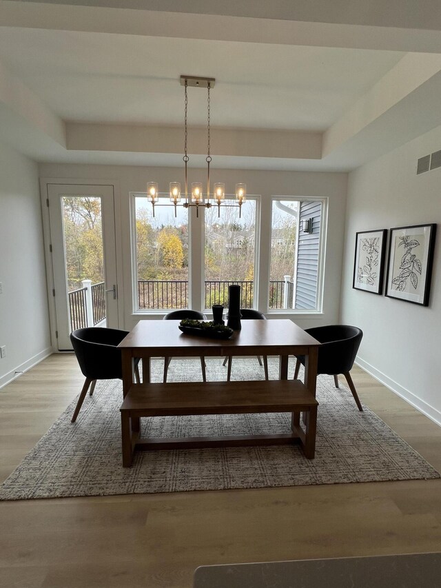 dining space featuring a tray ceiling, light hardwood / wood-style floors, and an inviting chandelier