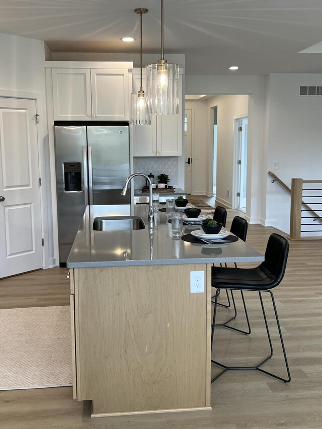 kitchen with white cabinets, decorative light fixtures, light hardwood / wood-style floors, and a kitchen island with sink