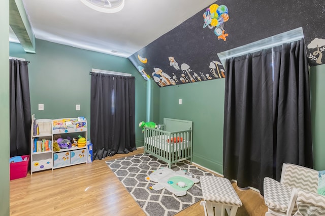 bedroom with a crib, hardwood / wood-style floors, and lofted ceiling