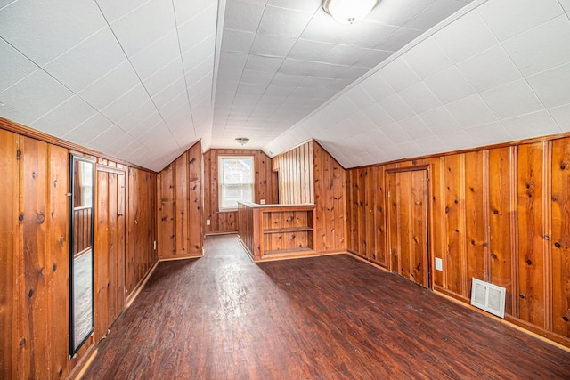 additional living space with dark hardwood / wood-style flooring, lofted ceiling, and wood walls