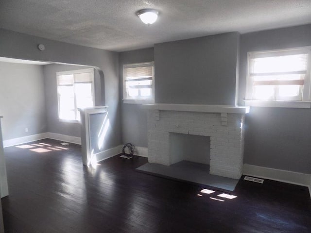 unfurnished living room featuring a fireplace, dark hardwood / wood-style flooring, a healthy amount of sunlight, and a textured ceiling