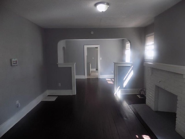 unfurnished living room featuring dark hardwood / wood-style floors, a textured ceiling, and a brick fireplace