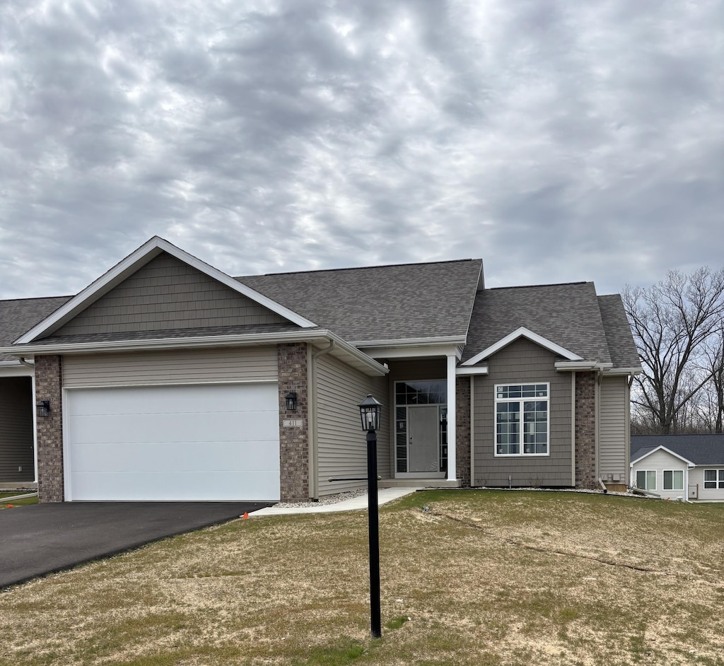 single story home featuring roof with shingles, brick siding, driveway, and an attached garage