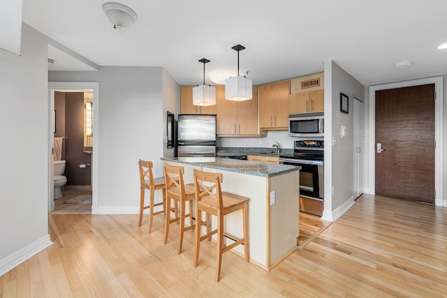 kitchen with a kitchen breakfast bar, light hardwood / wood-style flooring, dark stone countertops, decorative light fixtures, and appliances with stainless steel finishes