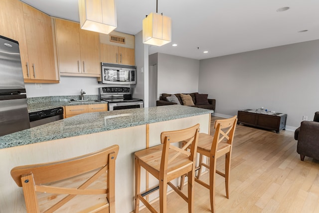 kitchen with light brown cabinetry, stainless steel appliances, stone countertops, light hardwood / wood-style floors, and a breakfast bar area